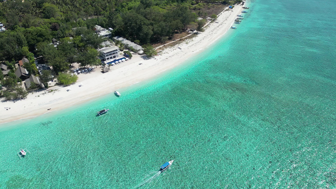 Luftaufnahme vom Meer mit Boot und Hotel Seri Resort Gili Meno im Hintergrund am Strand